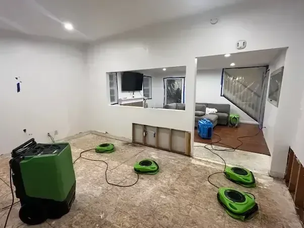 A dehumidifier and air movers drying a stripped floor in a finished room
