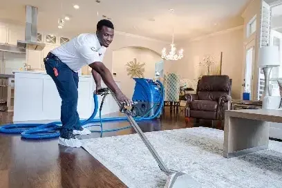 A technician running an extraction wand across a wet rug in a living room